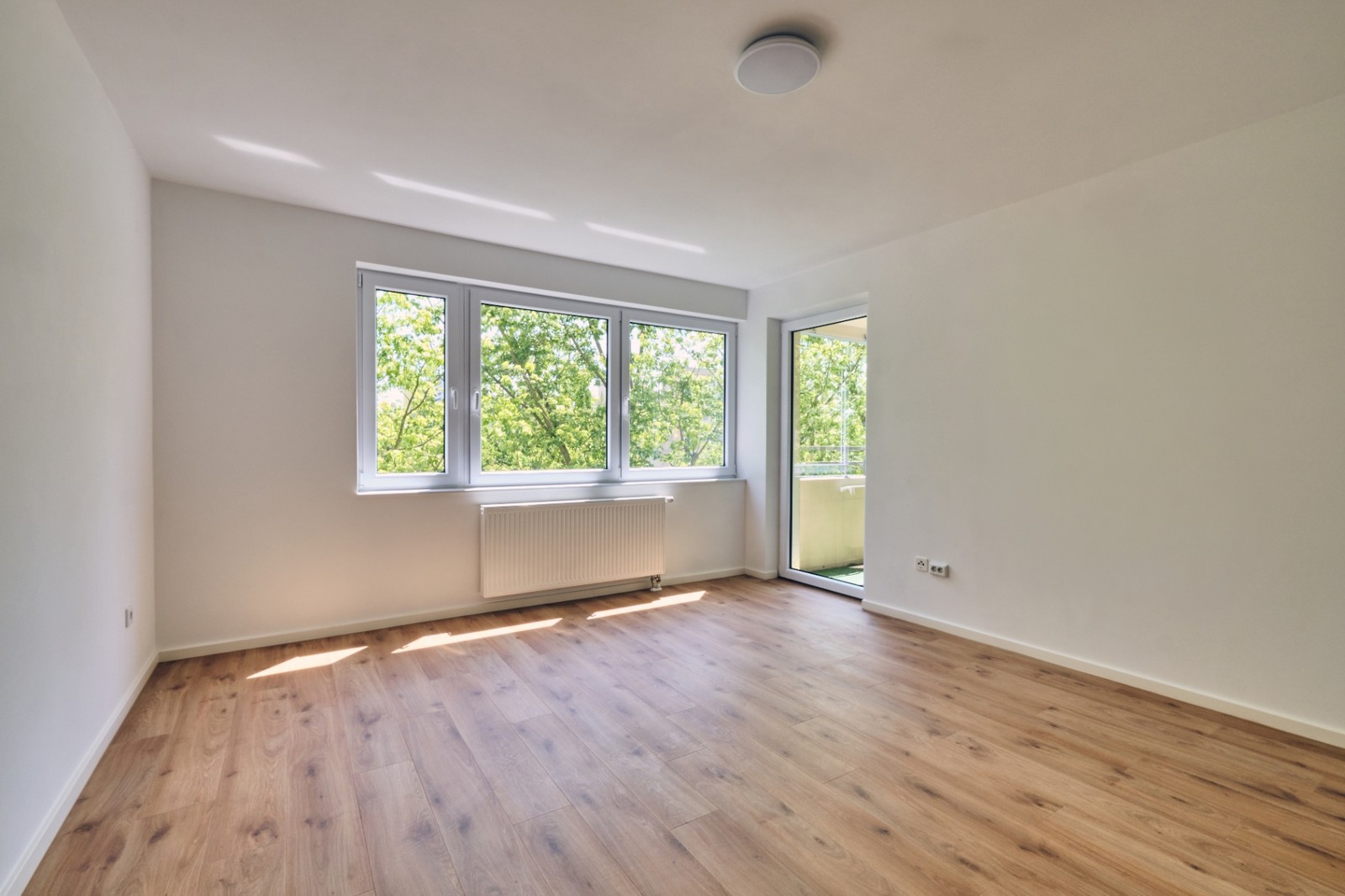 Heller Wohn-/Schlafraum mit großer Fensterfront, Balkonzugang und Blick ins Grüne